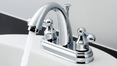 Silver bathroom faucet in white sink with water running