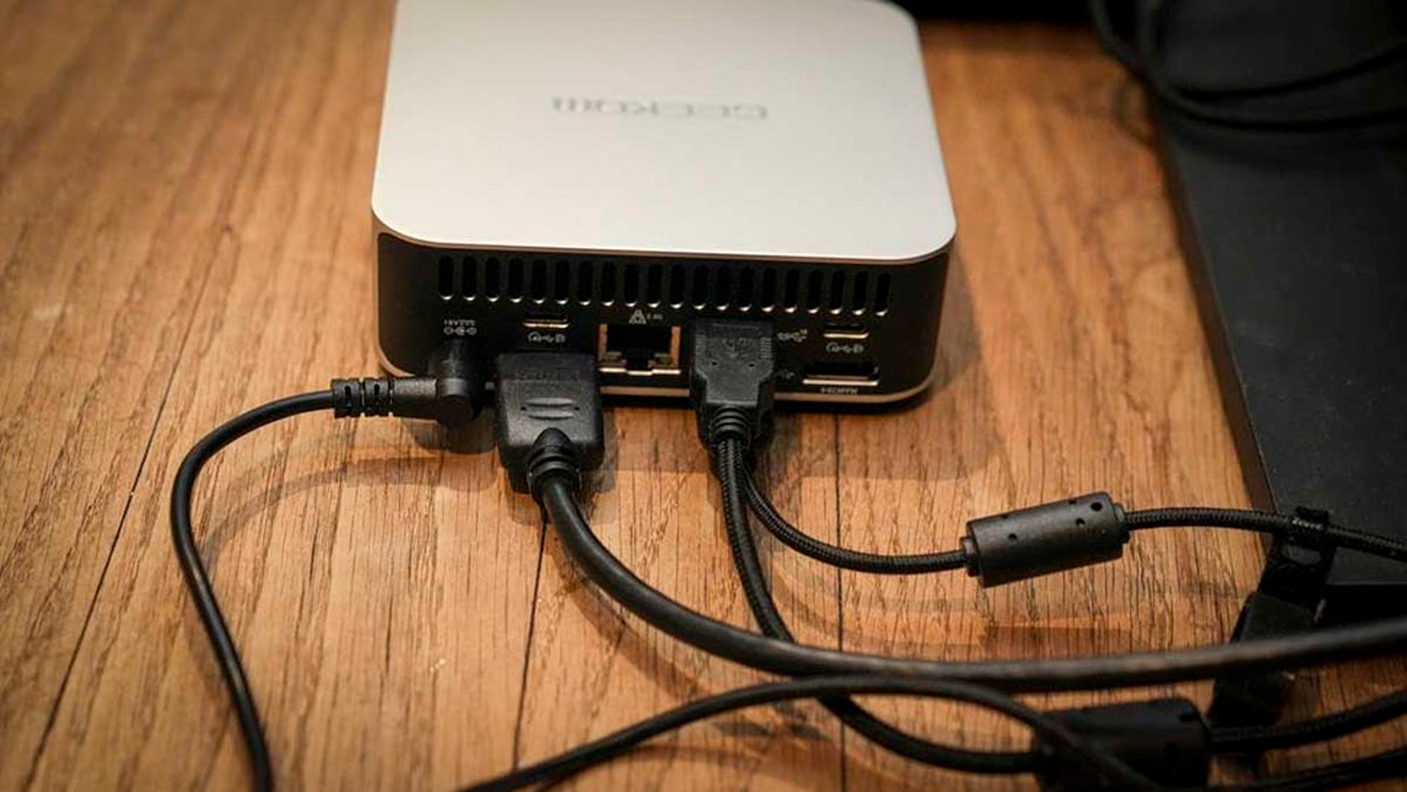 A small, silver-and-black computer hub with multiple cables plugged in sits on a wooden surface, conveying a sense of connectivity and technology.