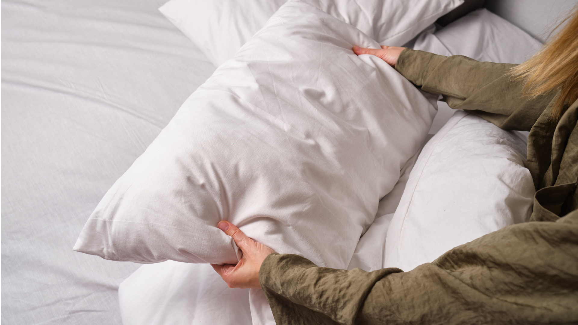 A woman holds a pillow as she makes her bed.