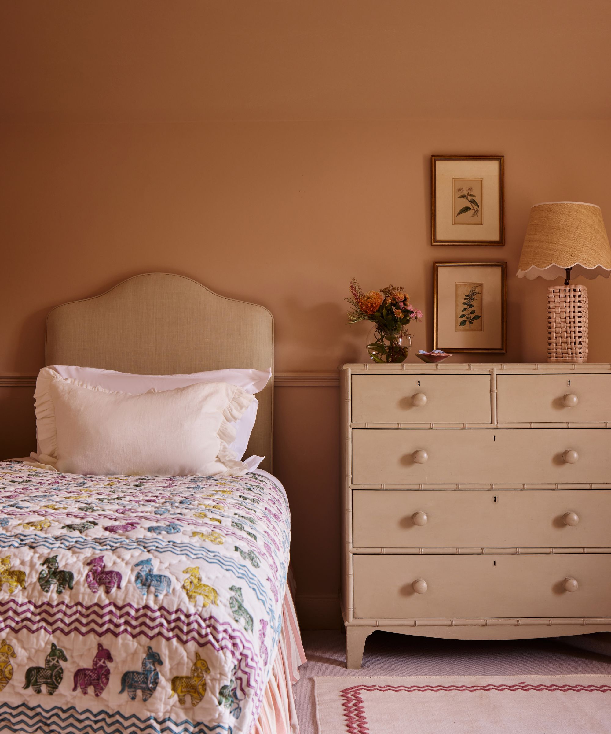 Warm terracotta bedroom featuring a single bed with a colorful horse-patterned quilt next to a classic cream chest of drawers