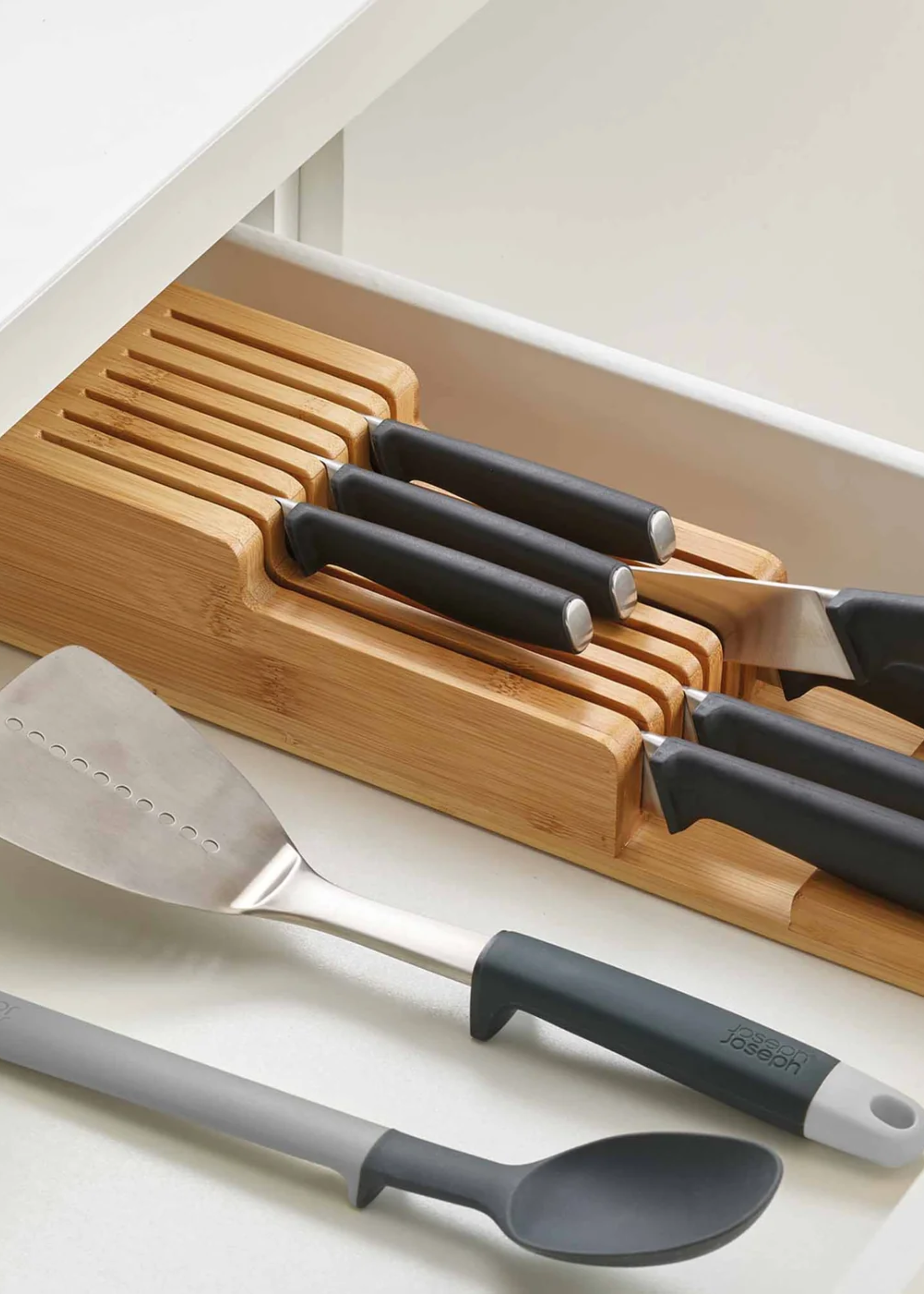A wood knife dock in a drawer near a ladle and a spatula