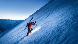 Skier ascends snowy alpine slope in early morning light