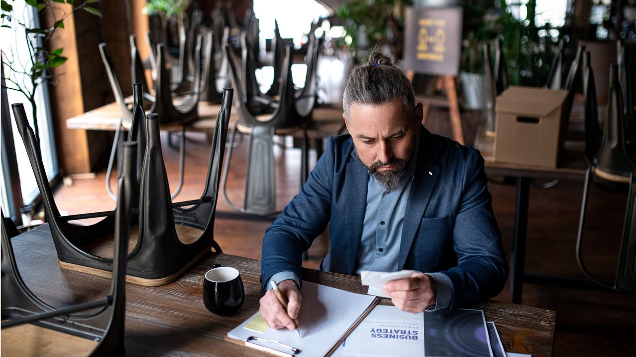 A small business owner looks over paperwork while sitting at a table in his restaurant.