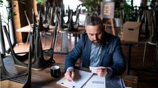 A small business owner looks over paperwork while sitting at a table in his restaurant.