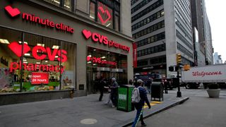 photo of the outside facade of a CVS Pharmacy in new york city as people walk past and a walgreens delivery truck drives by in the background