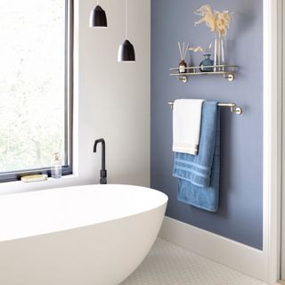 coastal bathroom with modern bath, blue wall, black pendant lights, towel radiator, white hex floor tiles, metal shelf, large crittall style window