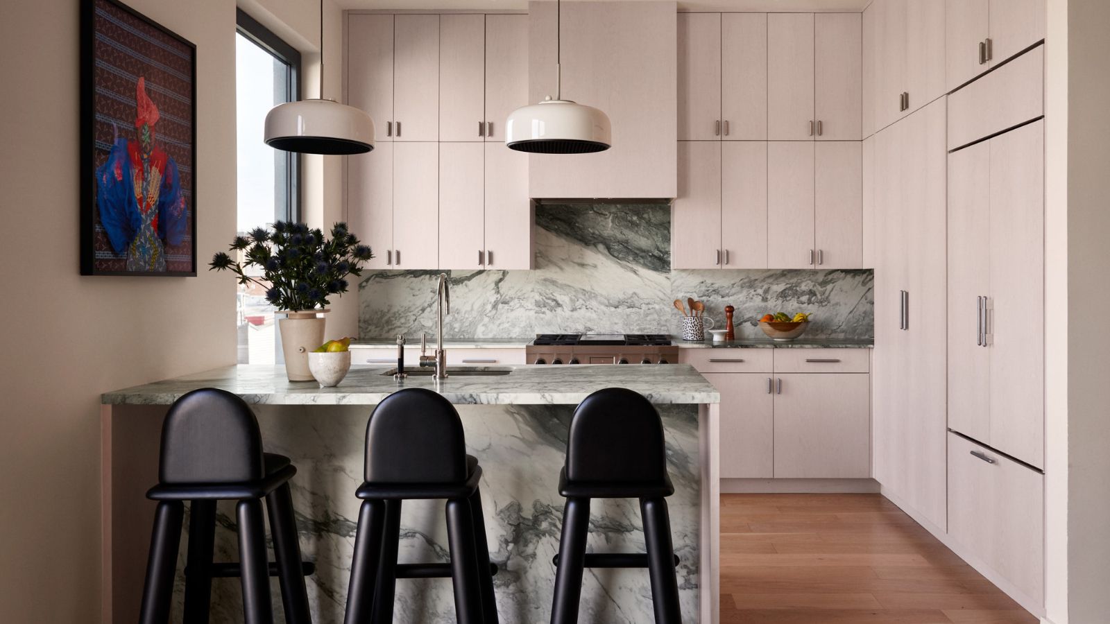 Kitchen with pink cabinets and marble island and backsplash, midcentury pendant lights and black bar stools