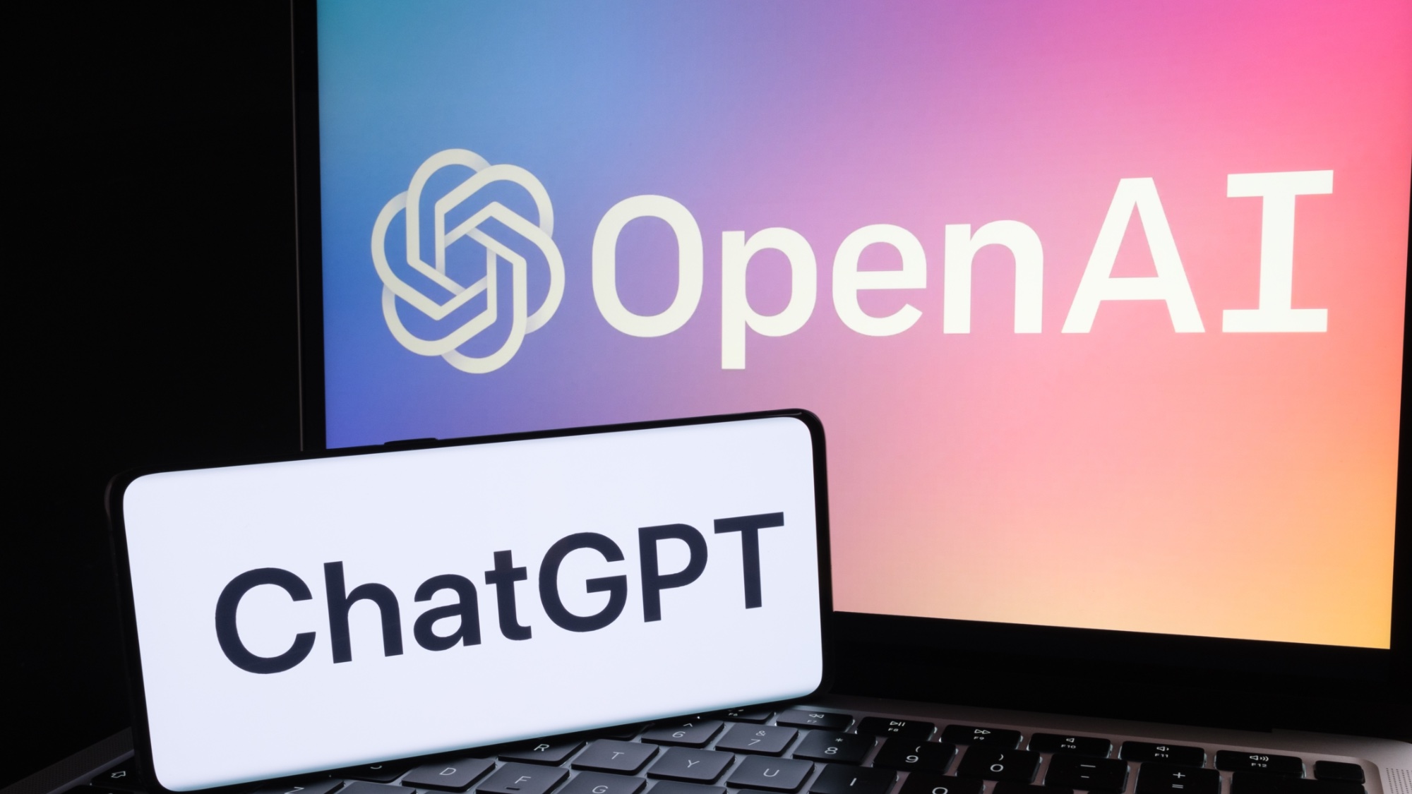 ChatGPT-Logo auf dem Telefon, das auf einem Laptop mit OpenAI-Logo sitzt