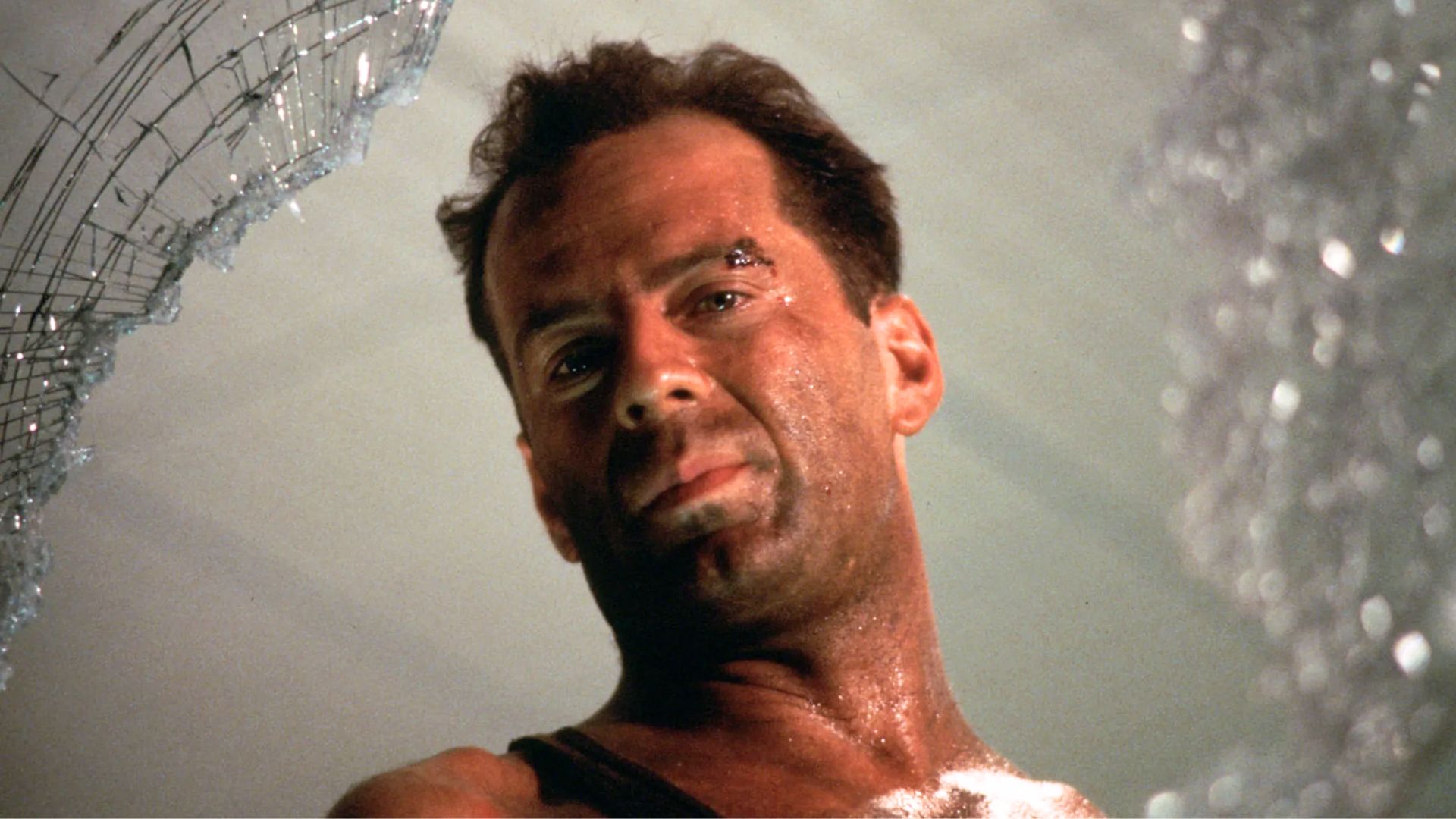 Bruce Willis como John McClane mira a través de una ventana rota durante Die Hard.