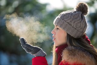 A woman watches her exhaled breath turn to steam in cold weather.