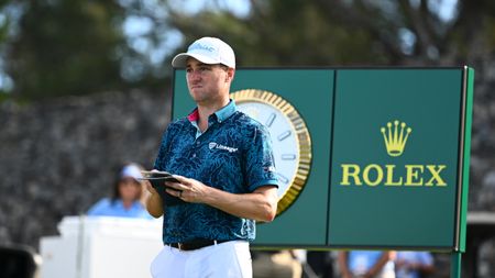 Justin Thomas looks at his yardage book with a large Rolex clock behind him at The Sentry 2025