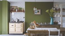 Farmhouse kitchen painted in Bancha by Farrow & Ball, white subway tiles, a cream range cooker, and a wooden dining table with a tablecloth and a blue enamel jug is filled with flowers.