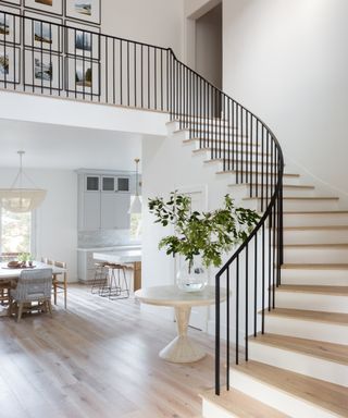 large hall with curved staircase and black balustrade and decor in neutral colors
