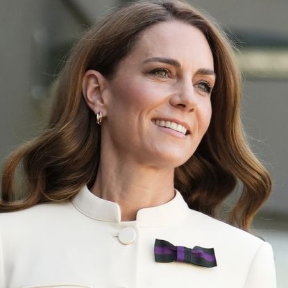 Kate Middleton has long brown wavy hair and wears a white dress