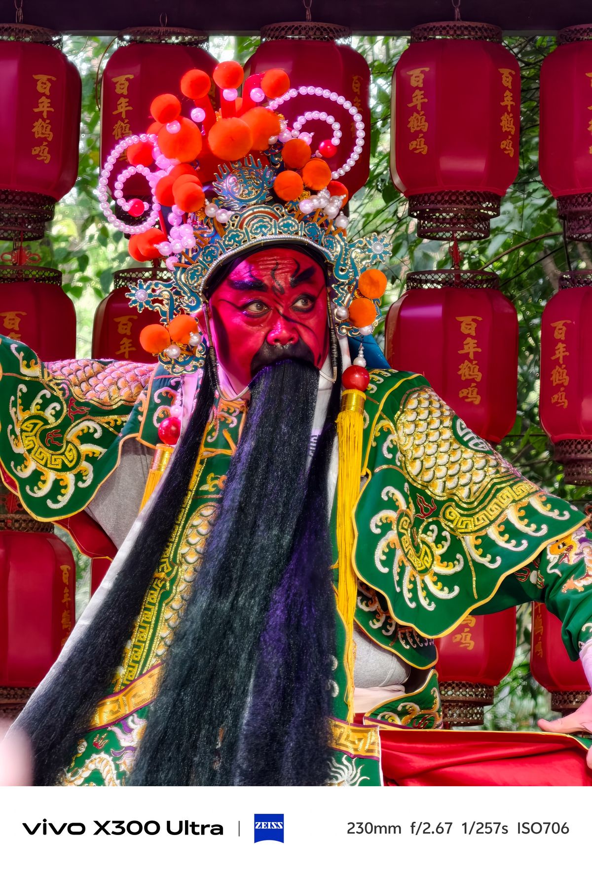 Close-up of a performer with a vibrant red mask and long black beard in a green costume.
