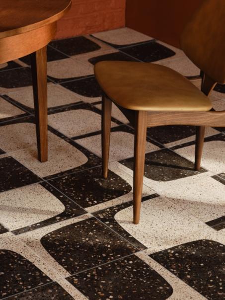 Close-up image of a black and white terrazzo flooring with a wooden a yellow leather chair.