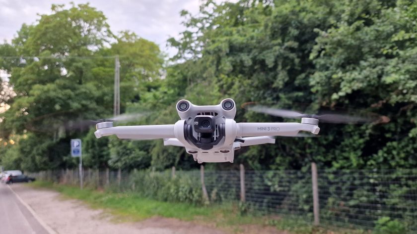 DJI Mini 3 Pro svæver i luften foran en grøn hæk og træer