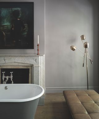 gray bathroom with roll top bath painted in dark gray, modern chaise, retro floor lamp, artwork, fire surround, candlestick