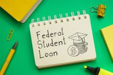 "Federal Student Loan" written on notepad with illustration of graduation cap and coins surrounded by yellow desk accessories against a green background