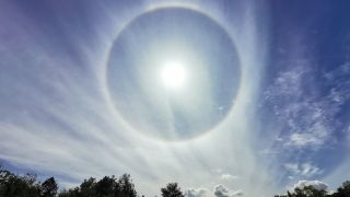 A large ring surrounds the sun in the sky accompanied by wispy clouds.