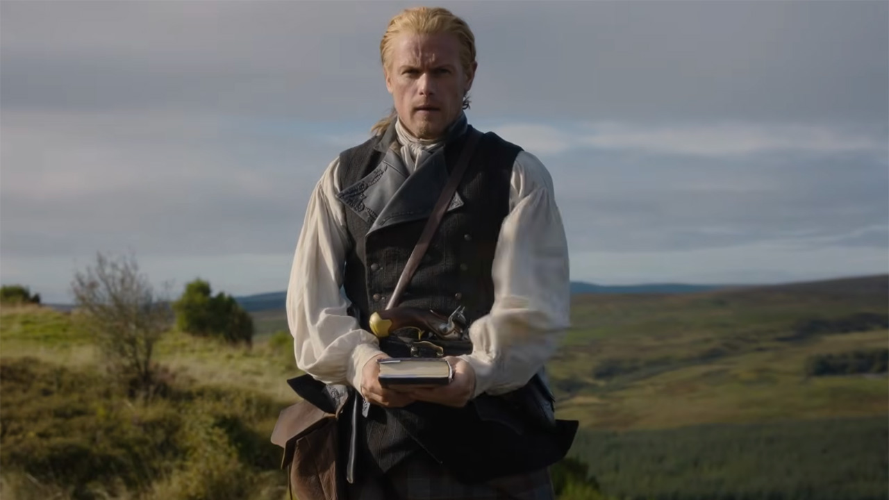 Sam Heughan standing on a hill holding a revolutionary musket in Outlander Season 8 trailer.