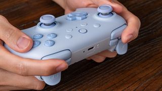 A marketing image of the Blue 8BitDo Ultimate 2C controller being held