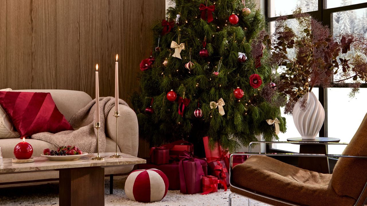 Living room with Christmas tree, red cushion on sofa and lit candles on coffee table