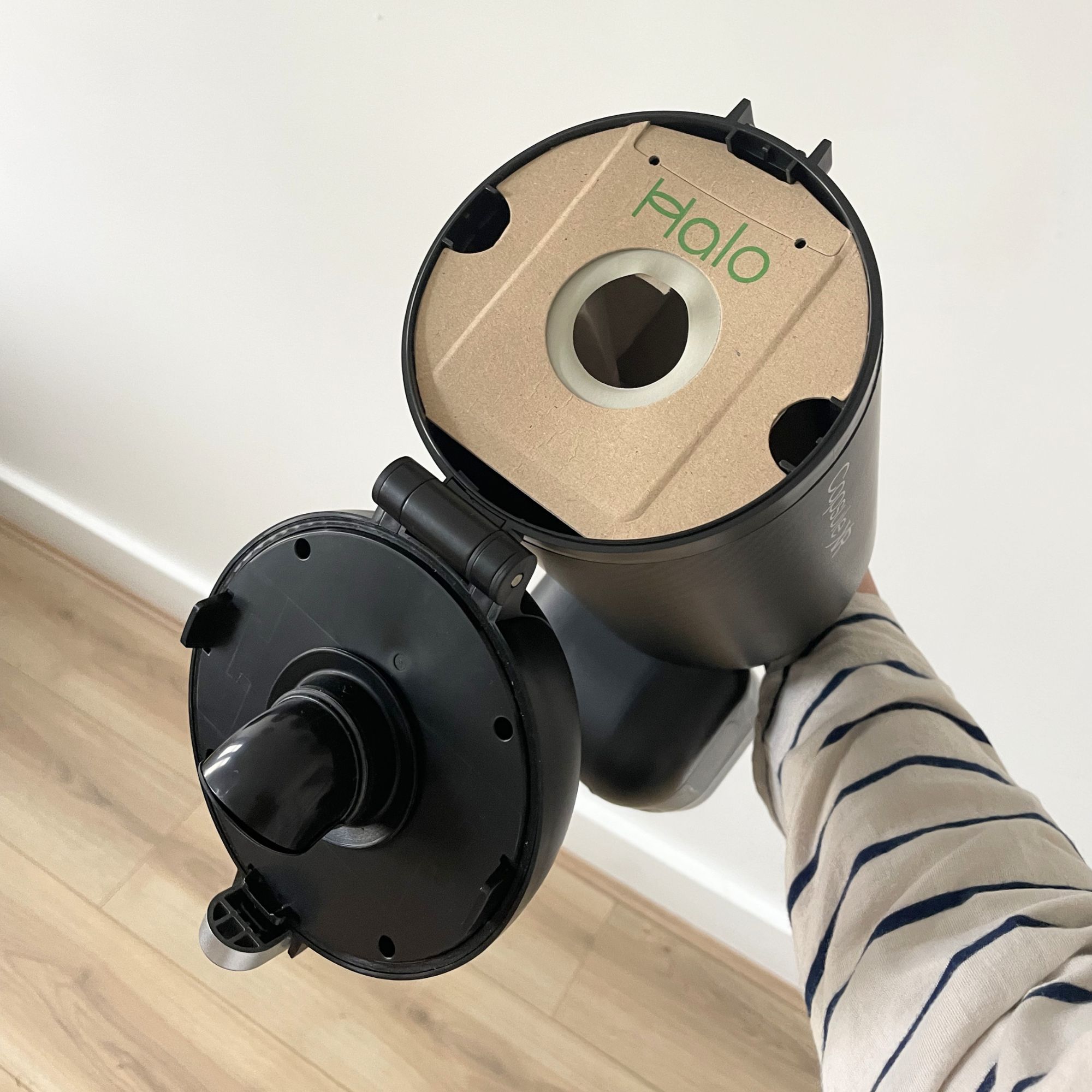 Hand holding the dust canister of the Halo Capsule XR, showing the brown dust bag inside