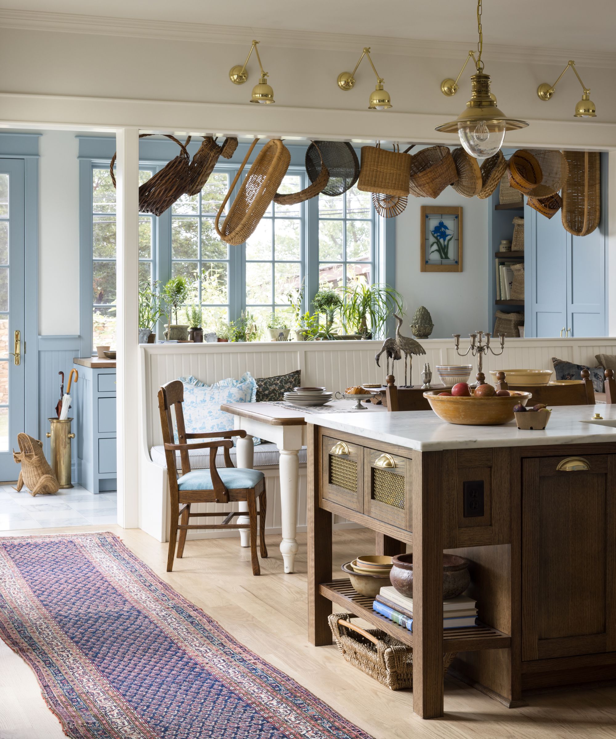 a cottage style southern kitchen with a dark wooden island, banquette seat, hanging baskets and a view through to a pale blue mudroom beyond