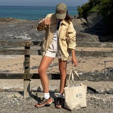 a woman wearing an olive green baseball cap, tan jacket, and chunky sneakers