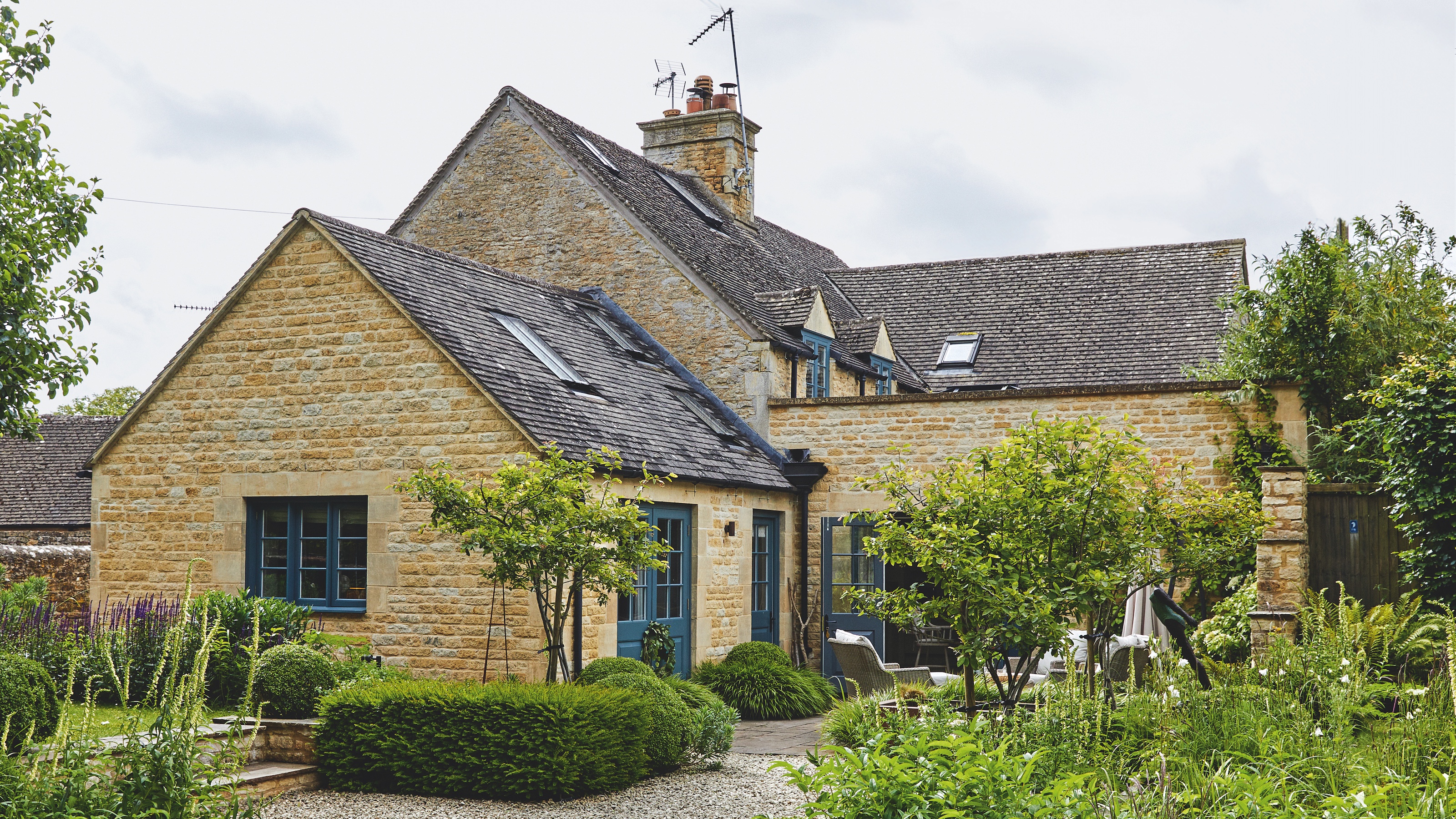 exterior of extended stone cotswold cottage with landscaped garden and gravel driveway