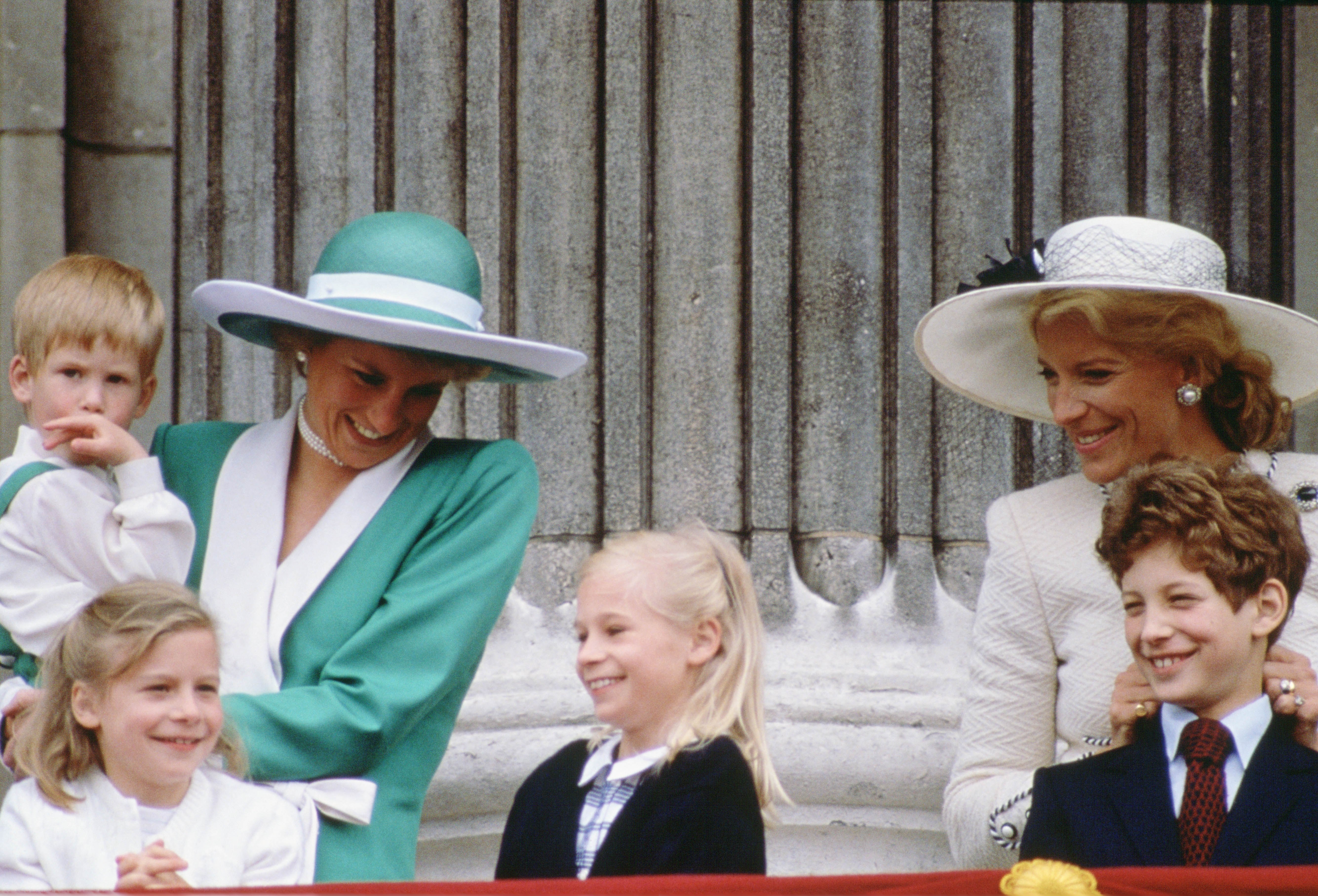 Princess Diana wears a green dress while holding a young Prince Harry in her arms as she watches Trooping the Colour with Princess Michael of Kent on the balcony of Buckingham Palace in June 1988
