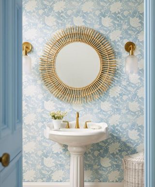 Blue and white coastal-inspired bathroom with a rattan wall mirror, white freestanding sink, and gold wall sconces