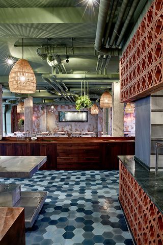 Restaurant with tables, chairs, wooden bar, patterned coloured walls, blue checkered flooring and large pendant lights at Bar Skuka, Frankfurt, Germany.
