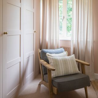 a bedroom with fitted wardrobes and a grey upholstered occasional chair beside a window with voiles