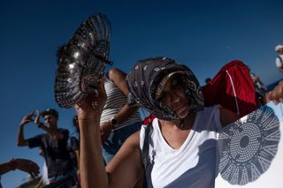a woman holds up a colander to the sun and projects the sun onto a white background.