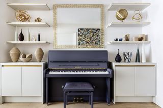 white living room/music room with piano in-between custom cabinets and shelving, mirror above piano