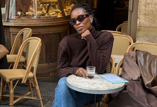 woman in brown turtleneck, jeans, and loafers at a cafe