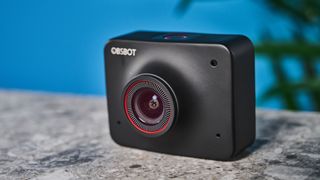 a black small 4K webcam with a red button photographed on a beige surface against a blue background