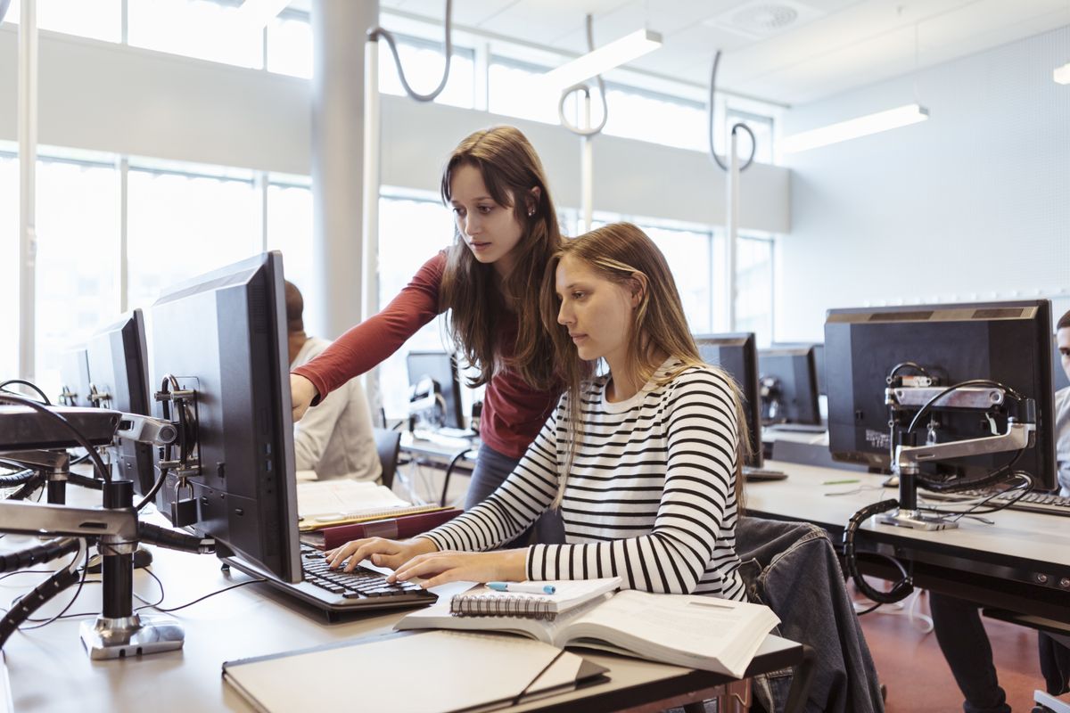 Female student on computer in library being helped by teacher