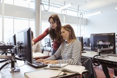 Female student on computer in library being helped by teacher
