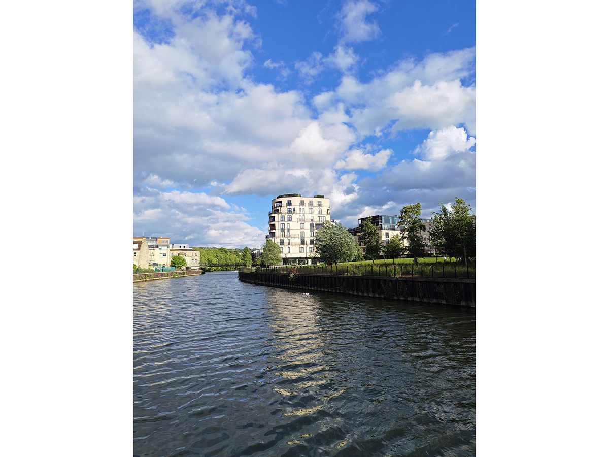 A tall block of flats by a river at a 1x zoom.