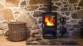 A log burner against a stone wall with a basket beside it