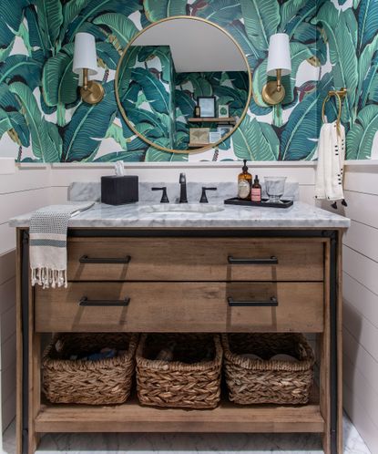An example of powder room wall decor showing a powder room vanity area with wooden drawers, a marble worktop and green palm print wallpaper