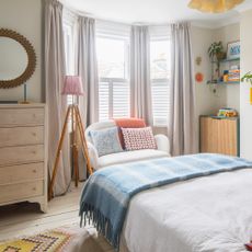 A bedroom with a bay window dressed with grey floor-length curtains and half-height shutters