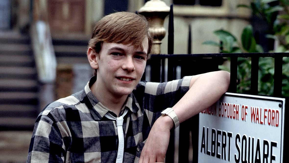 A young Ian Beale standing next to the Albert Square sign on the set of EastEnders.