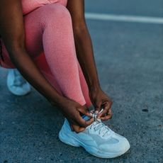 A woman tying up her shoelace in running kit while trying the viral jeffing running method