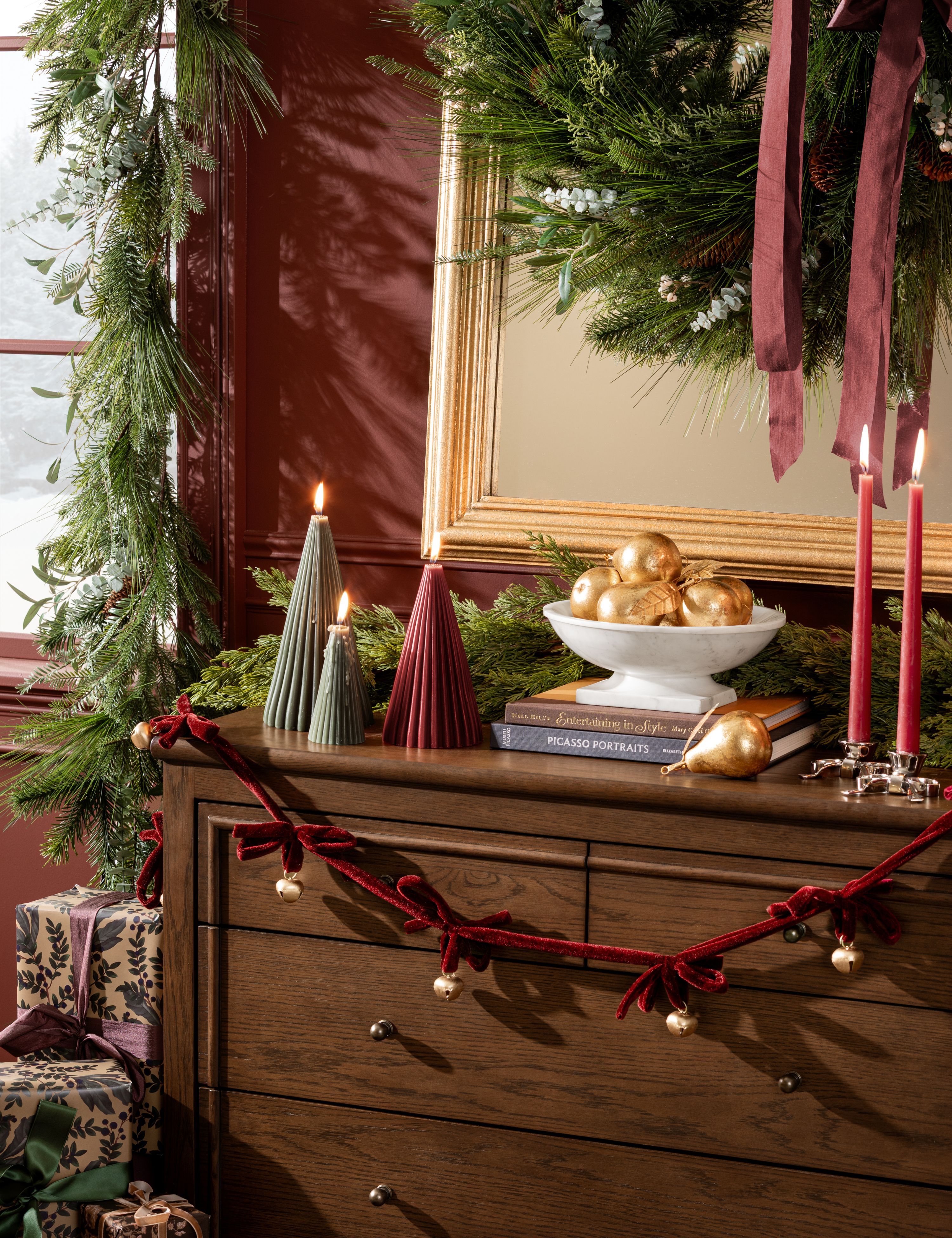 Bow-and-bell velvet gardland draped overtop of a wooden dresser, which is topped with sculptural festive accents
