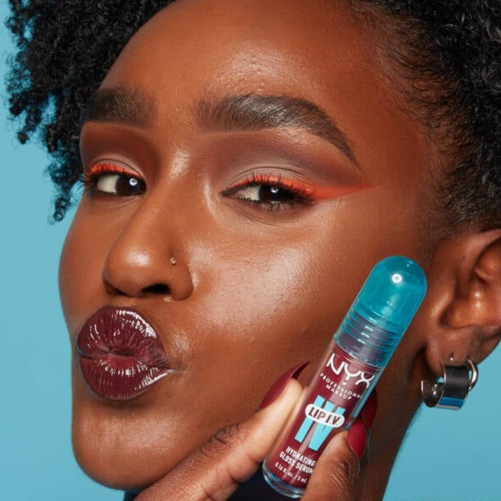 Woman with dark red lipstick and orange eyeline holding NYX Lip IV tint.