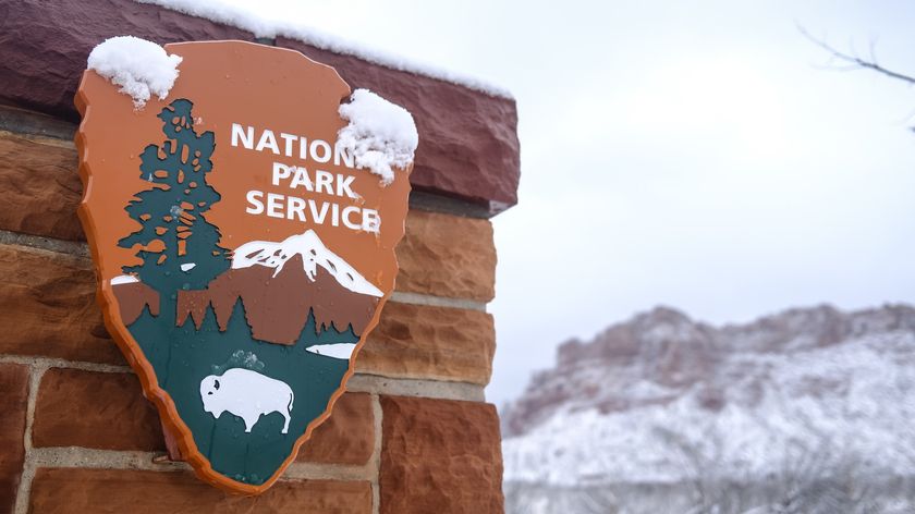 A National Park Service sign on a brick wall with snowy mountains in the background.